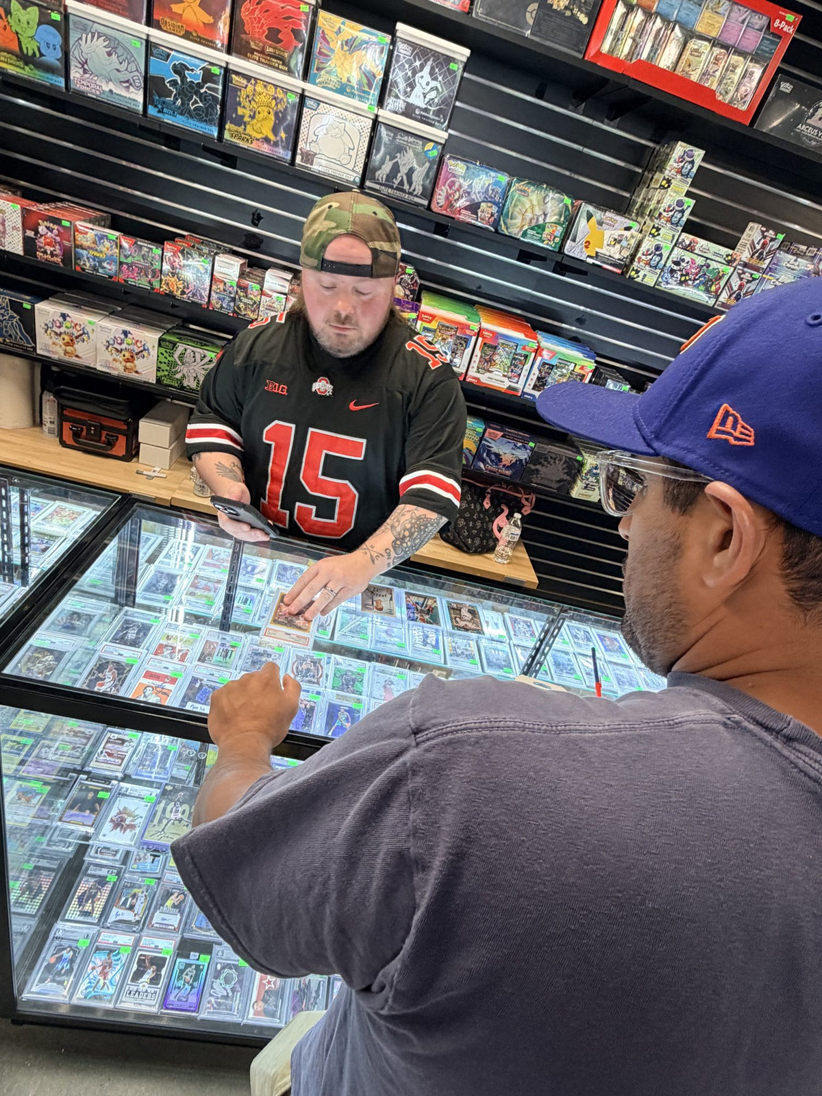B&B employee at a glass showcase full of graded slabs with the Pokémon wall behind