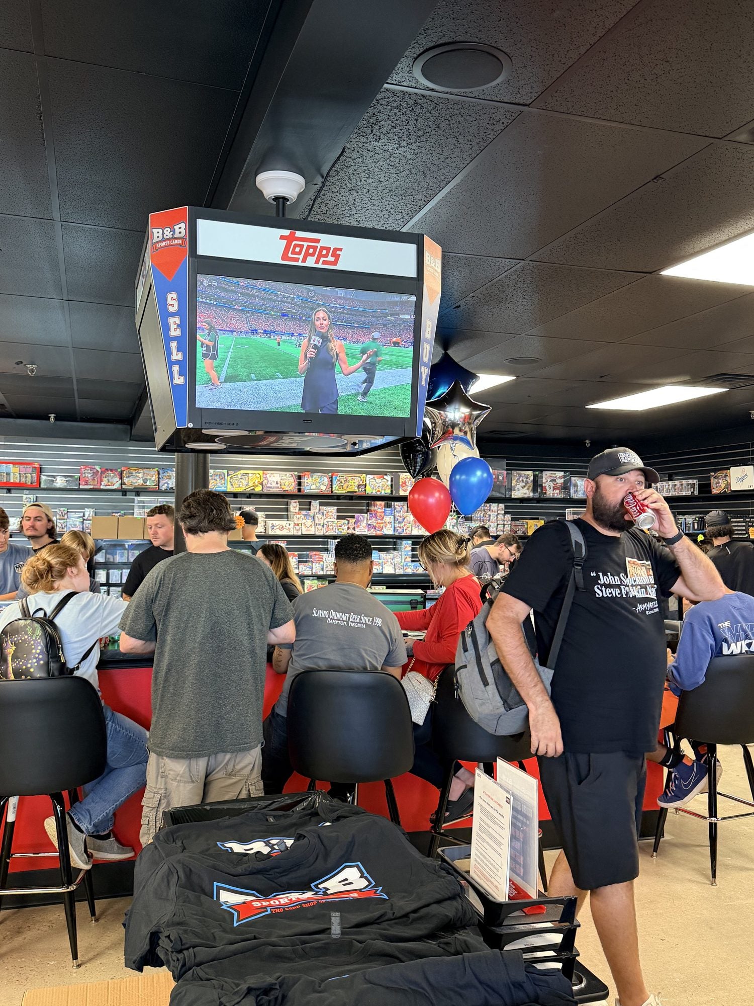 Packed B&B Sports Cards shop during the grand reopening, with balloons, the B&B Topps TV and customers at the red counter