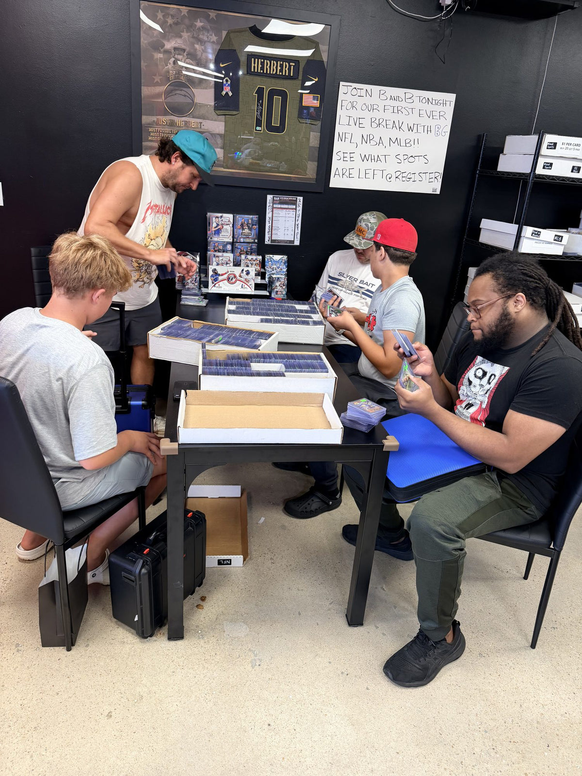Collectors ripping packs together at a table under a sign for B&B's first ever live break